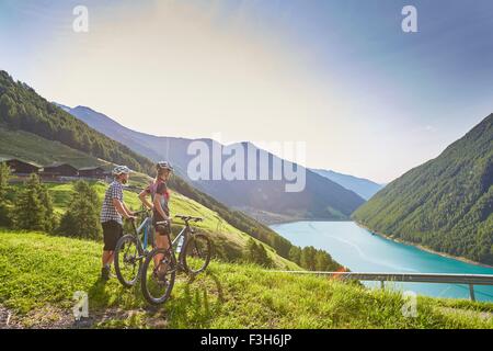 Young mountain biking couple looking out over Vernagt reservoir and Finailhof farmhouse, Val Senales, South Tyrol, Italy Stock Photo