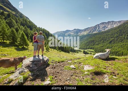 Rear view of young couple standing on boulder looking out to mountains, Val Senales, South Tyrol, Italy Stock Photo