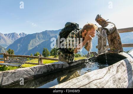 Young male hiker washing face in rustic trough, Karthaus, Val Senales, South Tyrol, Italy Stock Photo