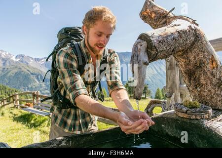 Young male hiker drinking water from rustic trough, Karthaus, Val Senales, South Tyrol, Italy Stock Photo
