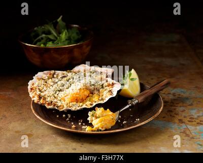 Still life of langoustine and prawn bake in seashell with bowl of mixed salad Stock Photo