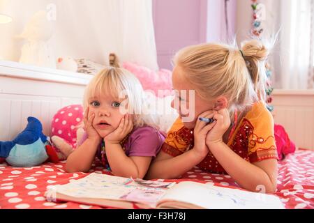 Girl and toddler sister on bed playing with colouring book Stock Photo