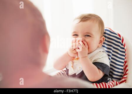 Baby boy feeding himself in baby chair Stock Photo