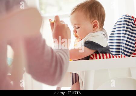 Mother feeding baby boy in baby chair Stock Photo