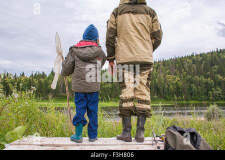 Father and son standing on jetty with fishing equipment, rear view Stock Photo