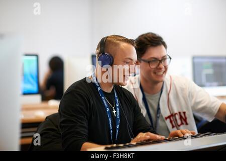 Male college student wearing headphones playing keyboards looking away smiling Stock Photo