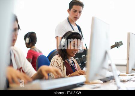 Female college student wearing headphones playing keyboards looking down smiling Stock Photo