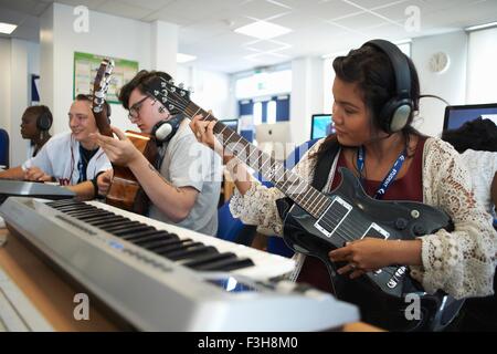 Small group of college students sitting in front of keyboards wearing headphones playing guitars Stock Photo