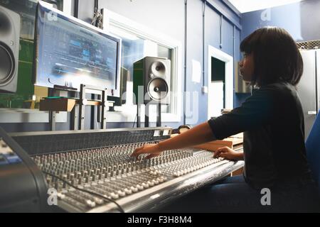 Side view of young woman sitting at mixing desk in recording studio looking at monitor, adjusting controls Stock Photo