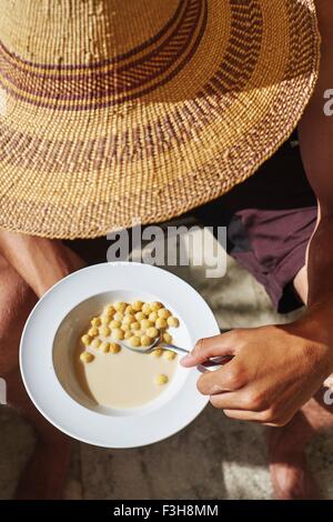 Cropped view of young man wearing sunhat eating breakfast cereal Stock Photo