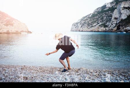 Rear view of young man skimming stones from beach, Javea, Spain Stock Photo