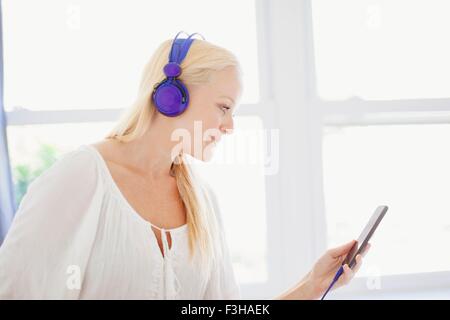 Side view of young woman looking at smartphone wearing headphones smiling Stock Photo