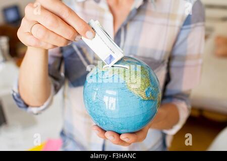 Cropped view of mature womans hands inserting money into globe money box Stock Photo