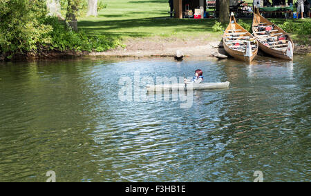 Teenage girl in kayak on Lake Ontario rows past two canoes and people having a bbq on Centre Island in Toronto, Ontario, Canada Stock Photo