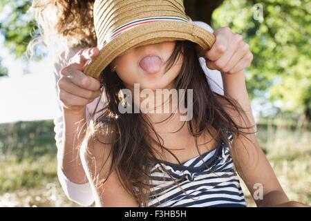 Mature woman covering daughters eyes with  straw hat in park Stock Photo