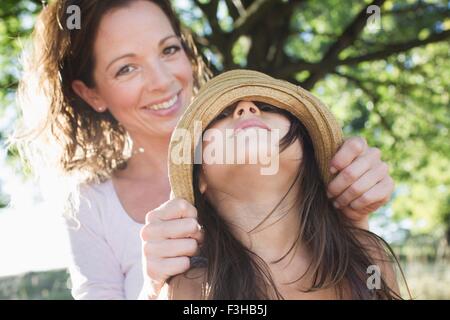 Portrait of mature woman covering daughters eyes with  straw hat in park Stock Photo