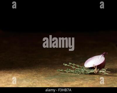 Still life of half a fresh red onion with fresh thyme tied with string on table Stock Photo