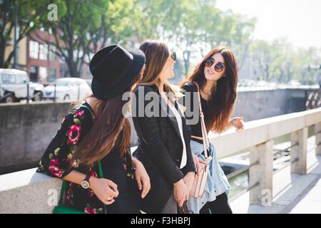 Three young female friends chatting on city riverside Stock Photo