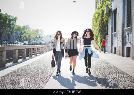 Three stylish young female friends strolling along sidewalk Stock Photo