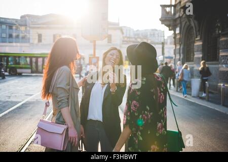 Three young women chatting and laughing on city street Stock Photo