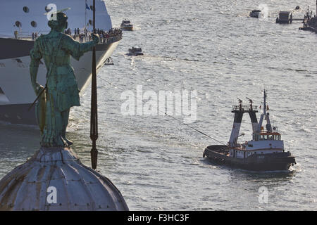 Giant cruise boat in Giudecca Canal towed by a tugboat and statue of Saint George on Basilica di San Giorgio Maggiore Venice Stock Photo