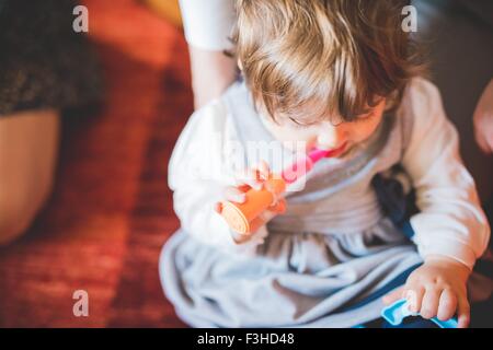 Female toddler sitting on living room floor playing with toy Stock Photo