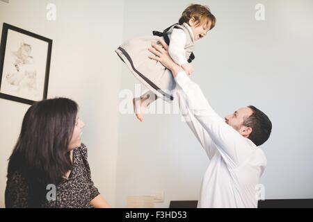 Mid adult man lifting up toddler daughter in living room Stock Photo