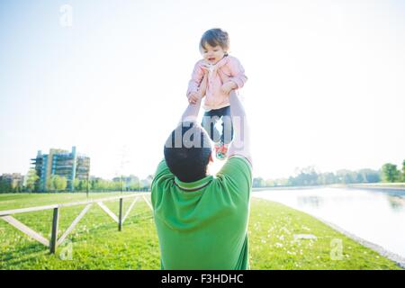 Mid adult man lifting up toddler daughter in park Stock Photo