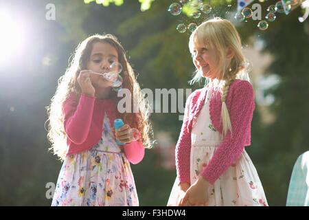 Two cute girls blowing bubbles in sunlit garden Stock Photo