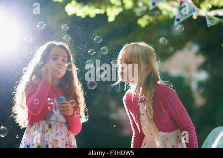 Two girls blowing bubbles in sunlit garden Stock Photo