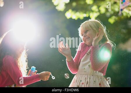 Two girls blowing and popping bubbles in sunlit garden Stock Photo