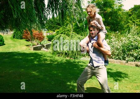 Mature man running with daughter on his shoulders in garden Stock Photo