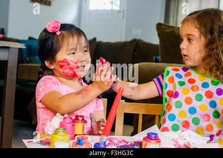 Two young girls sitting at table, making art, using paint Stock Photo