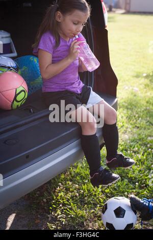 Girl football player sitting in car boot drinking water Stock Photo