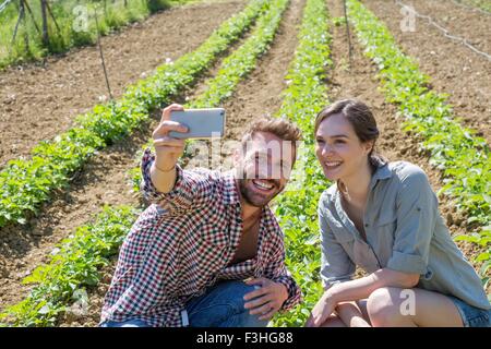 Young couple crouched in vegetable garden using smartphone to take selfie Stock Photo