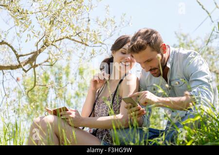 Low angle view of young couple sitting looking down at smartphone smiling Stock Photo