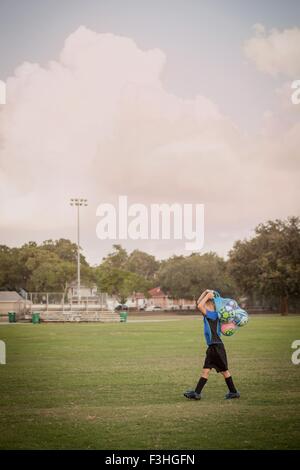 Boy football player carrying bag of footballs on practice pitch Stock Photo