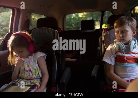 Boy watching younger sister using digital tablet in car back seat Stock Photo