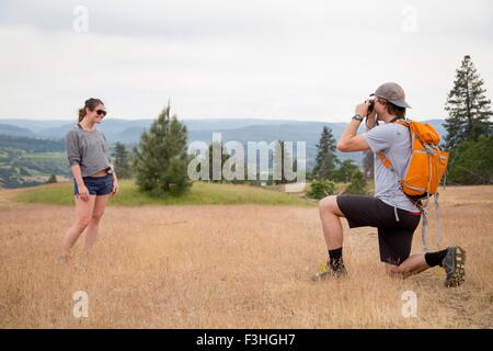 Young man taking photograph of young woman in rural setting Stock Photo
