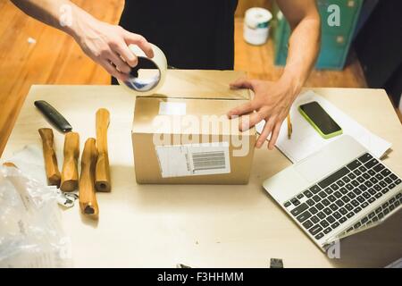 High angle view of young mans hands using sticking tape to prepare package for delivery Stock Photo