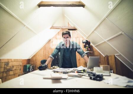 Young man leaning against desk in workshop looking at camera smiling Stock Photo