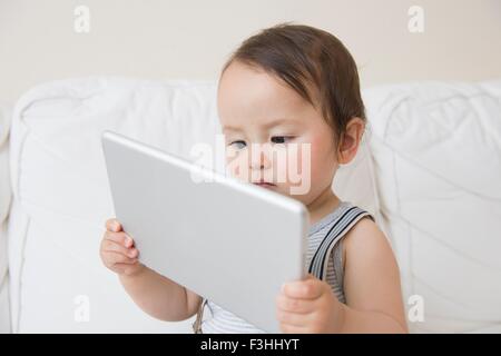 Baby boy sitting on sofa holding up digital tablet Stock Photo