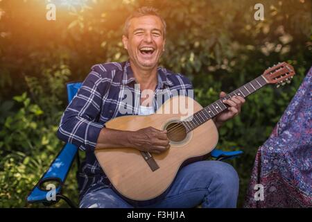 Portrait of mature man singing and playing acoustic guitar whilst camping Stock Photo