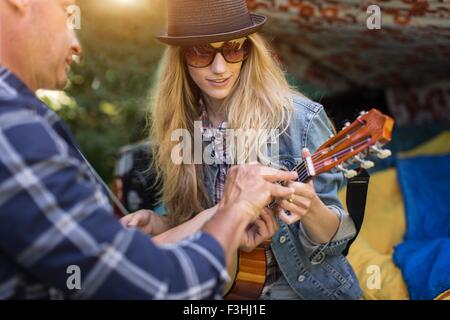 Mature man showing girlfriend how to play ukulele whilst camping in pick up boot Stock Photo