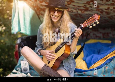 Portrait of young woman playing ukulele whilst camping in pick up boot Stock Photo