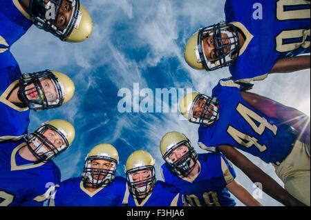 Low angle portrait of teenage and adult American football team against blue sky Stock Photo