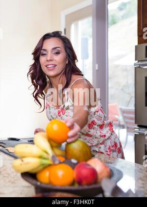 Mid adult woman picking up orange from fruit bowl Stock Photo