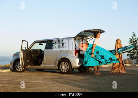 Couple taking surfboards from boot of car Stock Photo