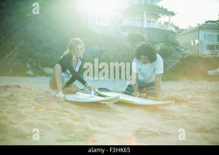 Couple sitting on beach, waxing surboards Stock Photo