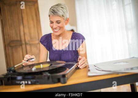 Happy mature woman playing vinyl on record player Stock Photo